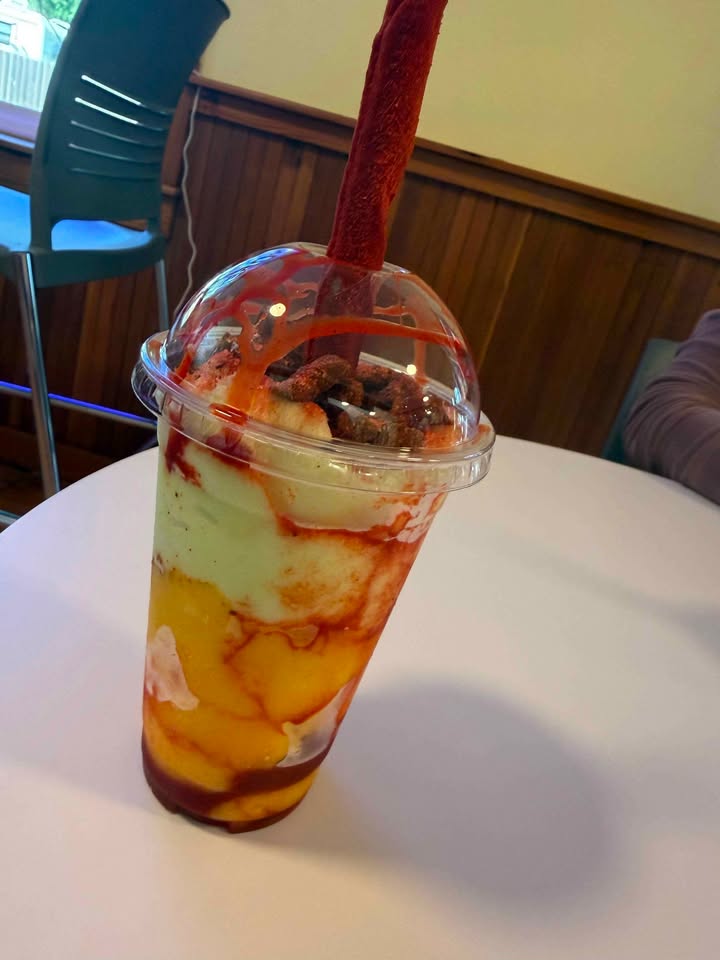 A layered mangonada with mango, chamoy, and a tamarindo candy straw